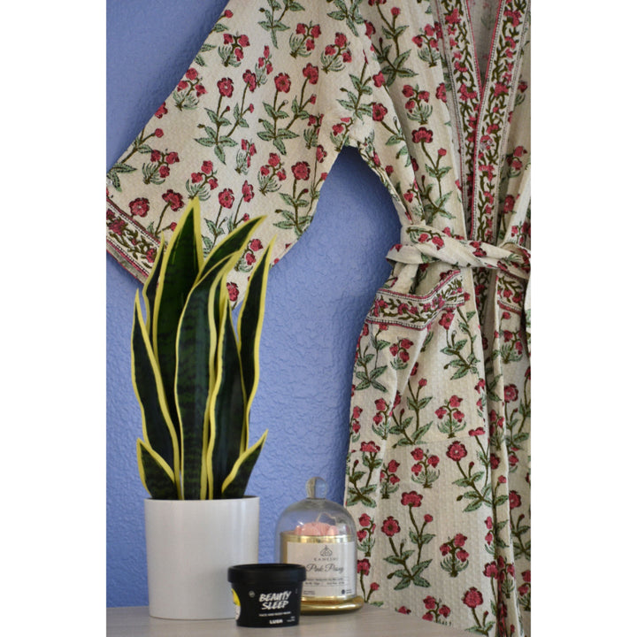 Close-up of pink vine handblock printed waffle cotton robe beside indoor plants and scented candles on a nightstand.