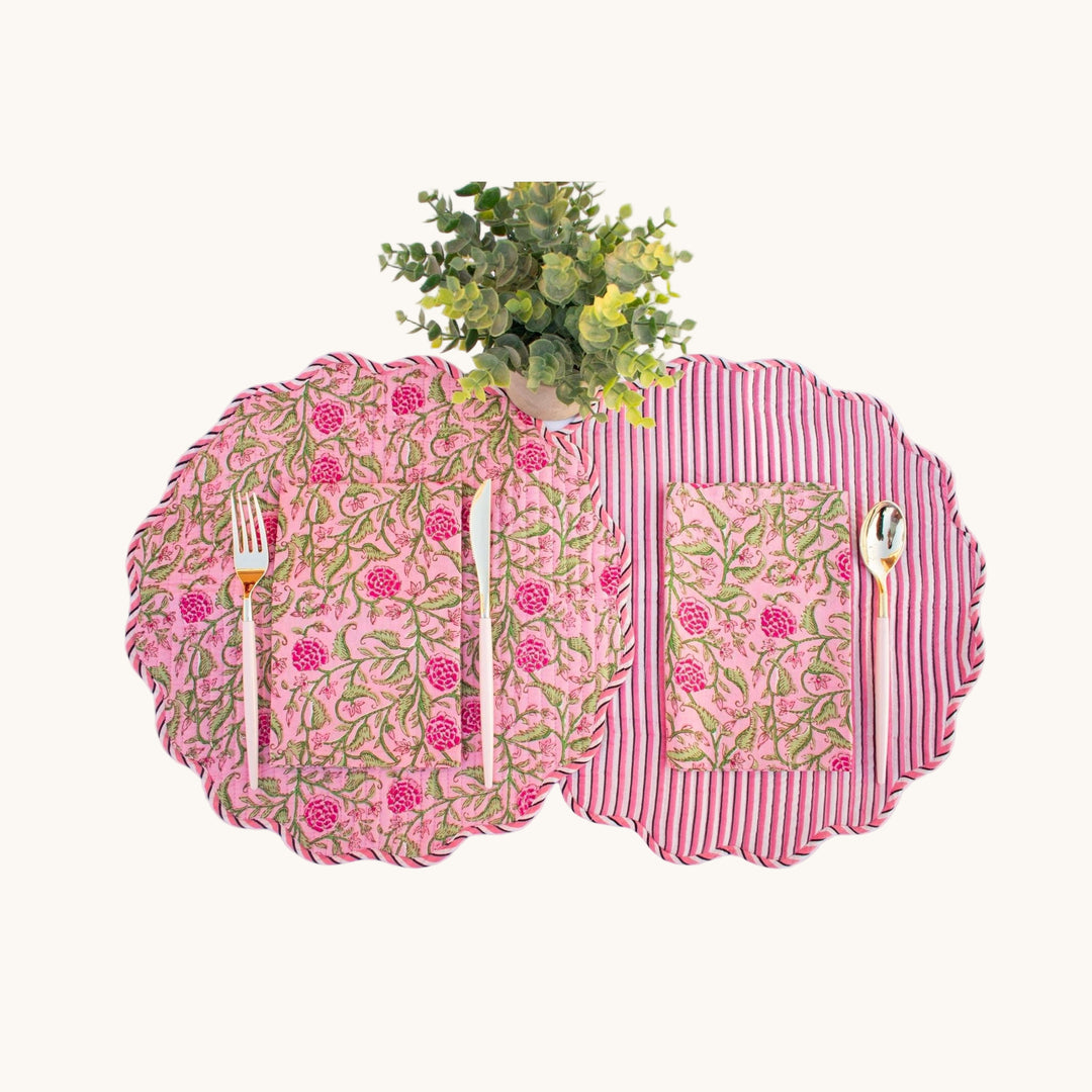 Reversible round quilted placemats with pink floral and red stripe prints, styled with cutlery and a plant.