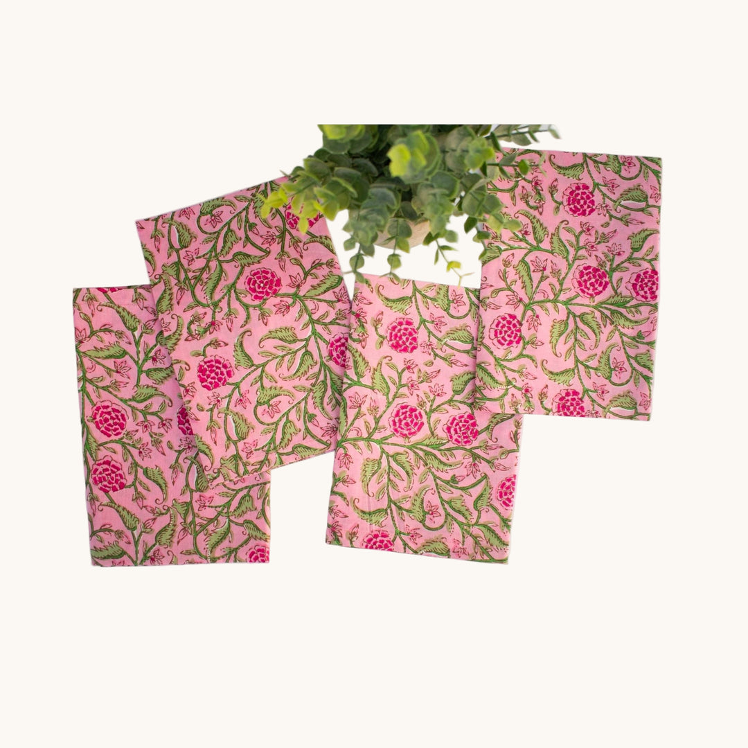 Set of four square cotton napkins with hand block printed pink floral design on a blush background, styled with greenery.