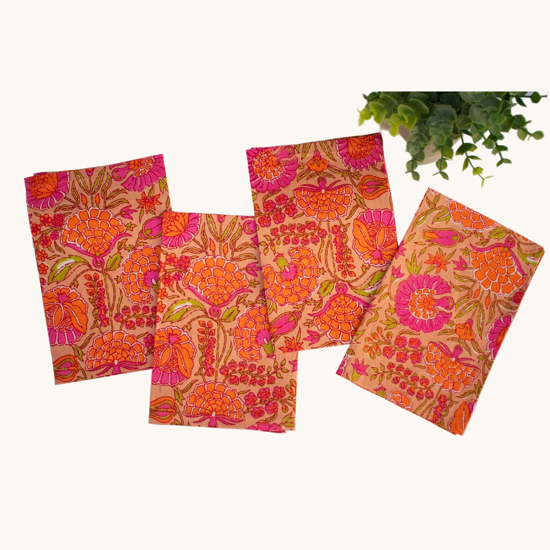 Set of four cotton napkins with bold orange, pink, and red floral block print, displayed flat with a potted plant.