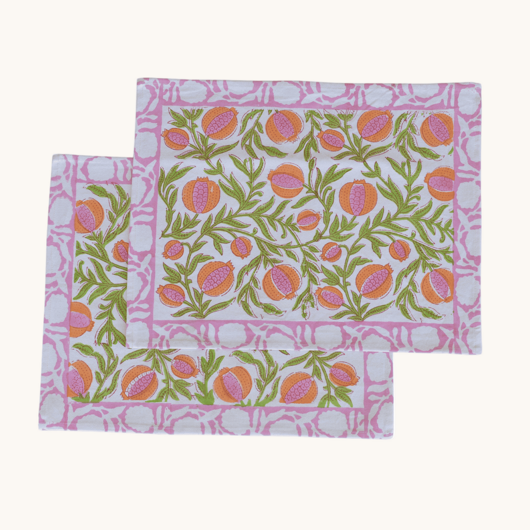 Rectangular cotton placemats with pink and orange pomegranate block print, bordered by a pink geometric pattern on a white background.