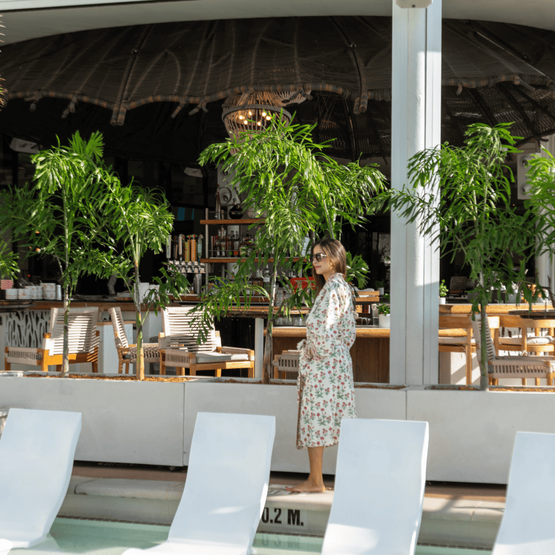 Woman in a floral robe standing in a modern outdoor restaurant with plants and white chairs.