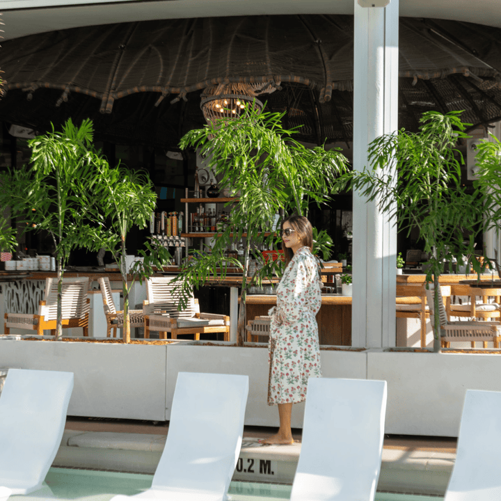 Woman in a floral robe standing in a modern outdoor restaurant with plants and white chairs.
