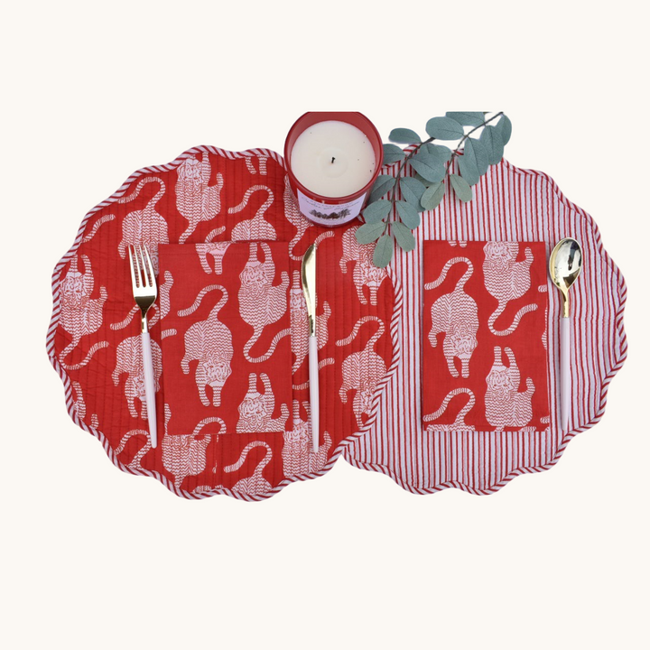 Reversible round quilted placemats with bold red and white animal print on one side and red stripes on the other, styled with cutlery, a candle, and eucalyptus.