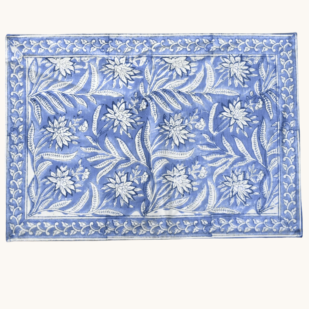 Rectangular cotton placemat with white floral block print on a dusty blue background, bordered with a matching floral pattern.