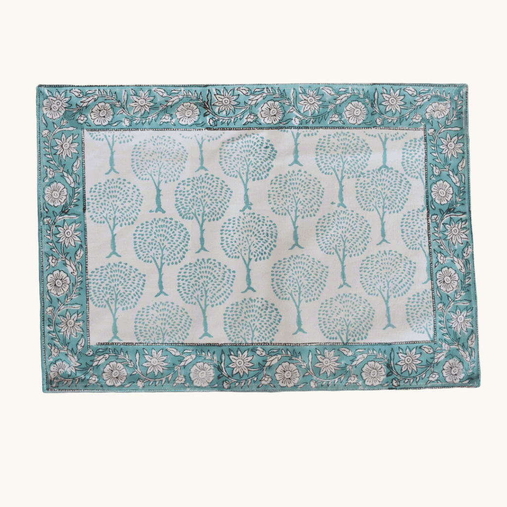 Rectangular cotton placemat with teal tree block print and a floral border, displayed on a wooden surface.