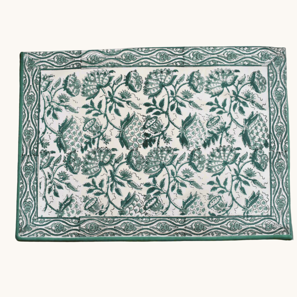 Rectangular cotton placemat with green floral block print and a decorative border, displayed on a wooden surface.