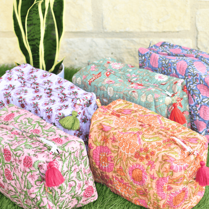 Colorful floral-patterned pouches with tassels on a grassy surface.