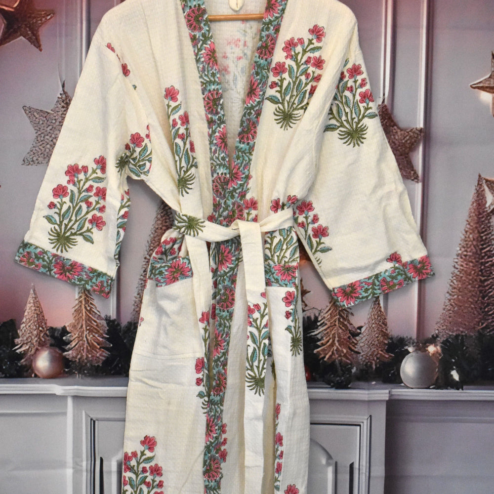 Blush Petal waffle cotton robe featuring handblock printed pink floral and green vine motifs on an off-white base, displayed against a festive holiday backdrop with metallic stars and miniature trees.